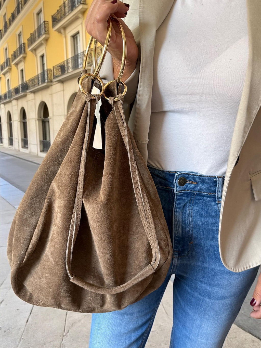 Close-up of sculptural 11cm gold-tone metal ring handles on a premium suede bag