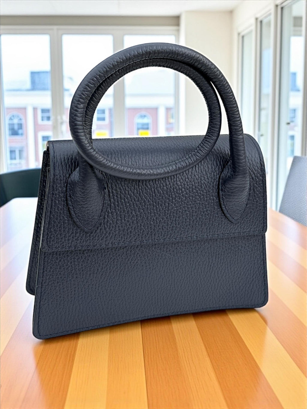 Front view of the navy blue pebbled leather trapezoidal handbag with gold hardware